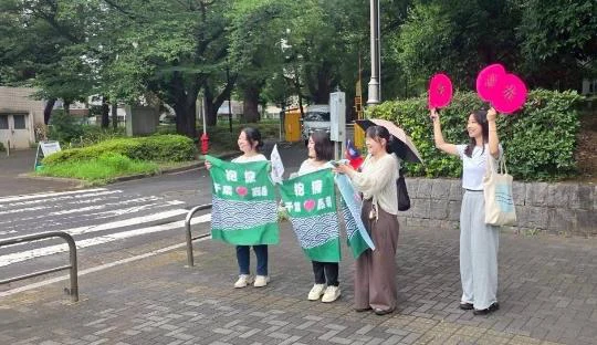 千葉大学の入口で、参加者が横断幕とうちわを持ち訪問者を迎える様子