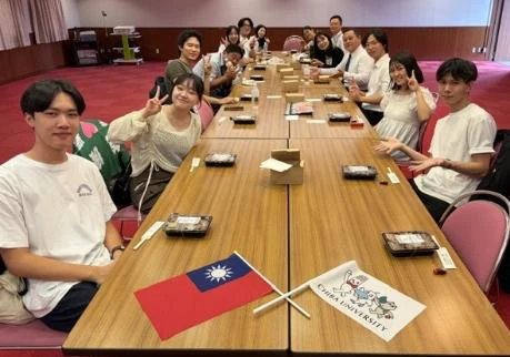 昼食の箱と交流の旗を並べた長いテーブルを囲む日台の参加者